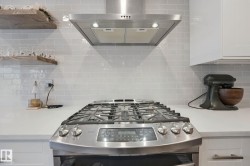 Stainless steel range with a built-in oven, stainless steel range hood, white subway tile backsplash, white countertops, and white cabinetry - 