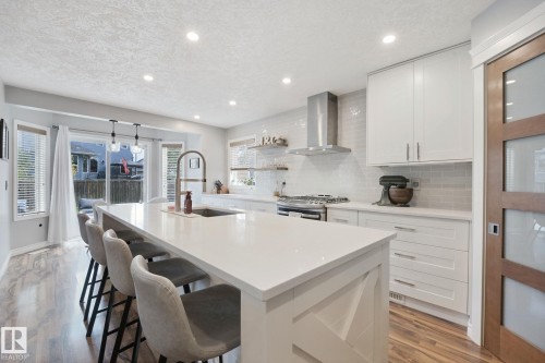 Kitchen featuring a large island with white countertop, wood-finish flooring, white cabinetry, stainless steel range hood, and sliding glass doors - 324 Ascott Crescent, Sherwood Park, AB 