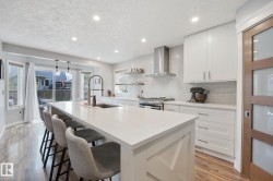 Kitchen featuring a large island with white countertop, wood-finish flooring, white cabinetry, stainless steel range hood, and sliding glass doors - 