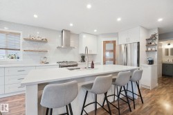 Spacious kitchen featuring an expansive island, white cabinetry, integrated stainless steel appliances, a tile backsplash, and wood-finish flooring - 