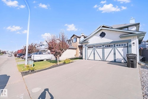 White siding exterior with a two-car garage featuring decorative doors, a concrete driveway, and landscaped front yard - 324 Ascott Crescent, Sherwood Park, AB 