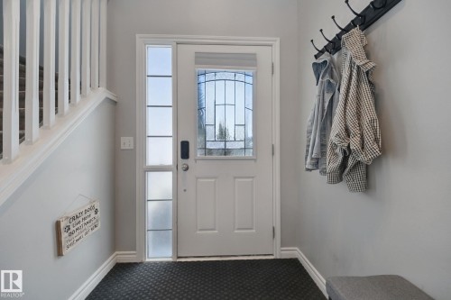 Entryway featuring a solid wood door with leaded glass, an adjacent sidelight with privacy glass, dark textured flooring, and a white staircase with balusters - 324 Ascott Crescent, Sherwood Park, AB 