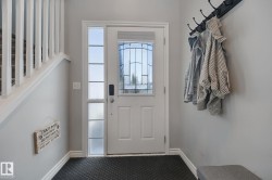 Entryway featuring a solid wood door with leaded glass, an adjacent sidelight with privacy glass, dark textured flooring, and a white staircase with balusters - 