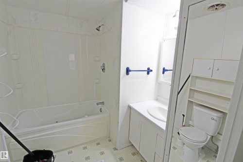 Bathroom featuring a white bathtub with shower, white vanity with integrated sink, white toilet, and built-in white storage shelving - #16 4202 45 St, Wetaskiwin, AB 