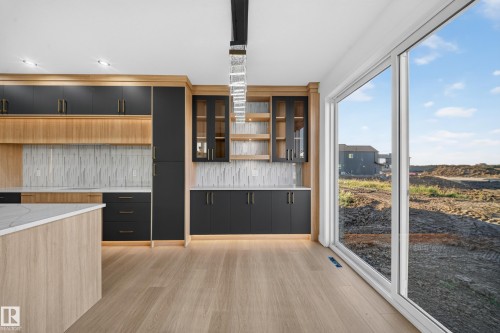 Kitchen featuring two-tone cabinetry with integrated lighting, a white textured backsplash, and a large central island with a light-toned countertop - 13024 186 Avene Nw, Edmonton, AB 
