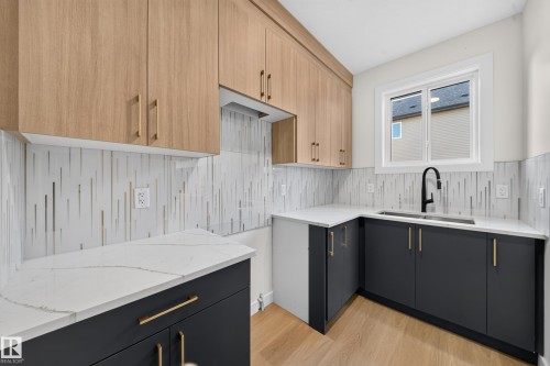 Two-tone cabinetry with wood-finish upper cabinets and dark lower cabinets, white countertops, modern backsplash, and a black gooseneck faucet - 13024 186 Avene Nw, Edmonton, AB 