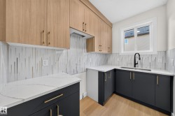 Two-tone cabinetry with wood-finish upper cabinets and dark lower cabinets, white countertops, modern backsplash, and a black gooseneck faucet - 