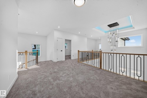 Carpeted hallway featuring a recessed ceiling fixture, contemporary chandelier, and decorative metal railings with wood accents - 13024 186 Avene Nw, Edmonton, AB 