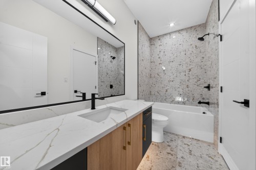 Vanity with quartz countertop and integrated sink, matte black faucet, full-width mirror, tile flooring, and a tiled shower with a bathtub - 13024 186 Avene Nw, Edmonton, AB 