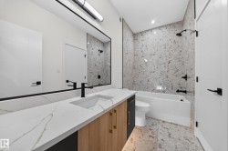 Vanity with quartz countertop and integrated sink, matte black faucet, full-width mirror, tile flooring, and a tiled shower with a bathtub - 
