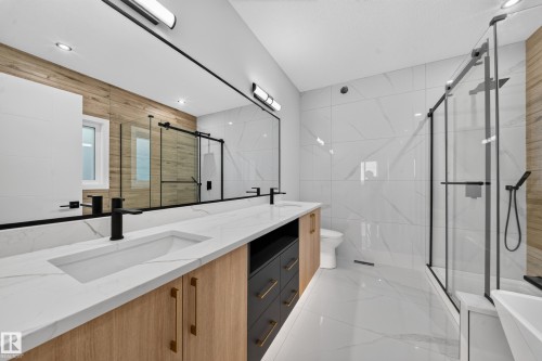 Dual vanity with integrated sinks and black matte faucets, expansive mirror with task lighting, wood-finish and dark cabinetry, large format wall and floor tiling, and a frameless glass shower enclosure - 13024 186 Avene Nw, Edmonton, AB 