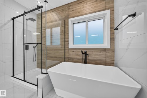 Freestanding soaking tub, walk-in shower with black-framed glass enclosure, wood-look wall tile, and large format marble-look wall and floor tile - 13024 186 Avene Nw, Edmonton, AB 