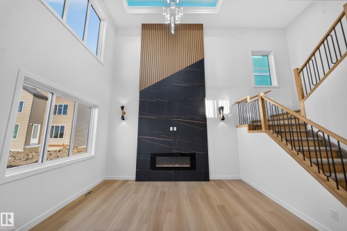 Two-story living area with wood-finish flooring, a contemporary fireplace with a dark stone-look surround and wood paneling, and a staircase with wood handrails and black metal balusters - 13024 186 Avene Nw, Edmonton, AB 