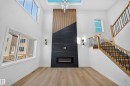 Two-story living area with wood-finish flooring, a contemporary fireplace with a dark stone-look surround and wood paneling, and a staircase with wood handrails and black metal balusters - 13024 186 Avene Nw, Edmonton, AB 