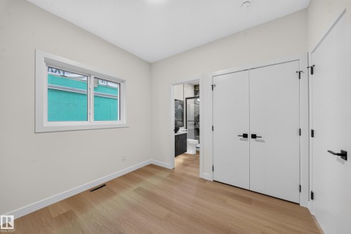Light wood-finish flooring, white walls, double-pane window, flush-panel doors with matte black hardware, and recessed ceiling lighting - 13024 186 Avene Nw, Edmonton, AB 