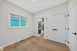 Light wood-finish flooring, white walls, double-pane window, flush-panel doors with matte black hardware, and recessed ceiling lighting - 