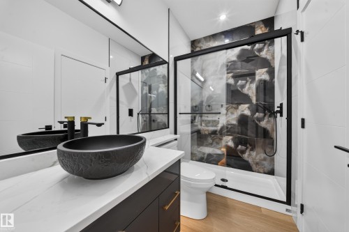 Black vessel sink with gold-finish faucets, white countertop, dark wood-finish vanity, glass-enclosed shower with black framing, and a tiled shower wall - 13024 186 Avene Nw, Edmonton, AB 