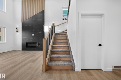 Two-story living area featuring wood-finish flooring, a contemporary fireplace with a black stone surround and wood paneling, and a staircase with wood treads, carpet runner, and black metal balusters - 13024 186 Avene Nw, Edmonton, AB 