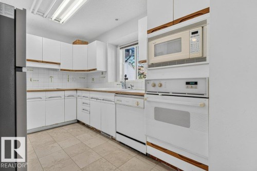 White cabinetry with wood trim accents, light-toned tile flooring, built-in microwave, and a wall oven - Edmonton, AB 