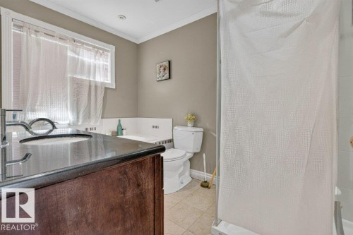 Bathroom featuring a dark wood-finish vanity with an undermount sink, a dark countertop, a window with white trim, a built-in tub, and tile flooring - Edmonton, AB 