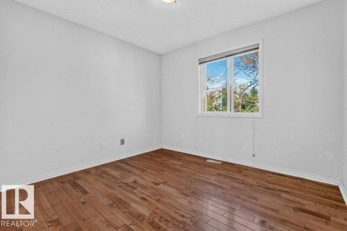 Bright, light-filled bedroom showcasing gleaming wood-finish flooring, pristine white walls, and a large window framing natural outdoor scenery - Edmonton, AB 