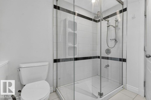 Glass-enclosed shower with white subway tile and decorative black accent bands, featuring a dual shower head system - Edmonton, AB 
