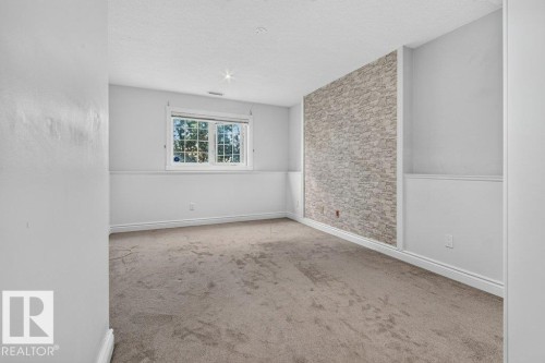 Carpeted room with a window, white trim, and a stone-clad accent wall - Edmonton, AB 