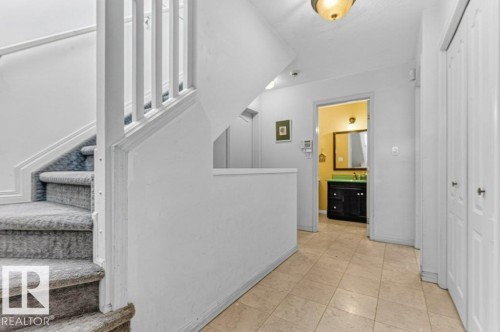 Carpeted staircase with white balusters, tiled flooring, and multiple closet doors - Edmonton, AB 