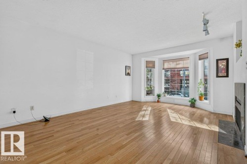 Hardwood flooring throughout, a bay window with multiple panes, a fireplace with a dark stone surround, a built-in wall niche, and track lighting - Edmonton, AB 
