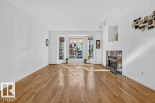 Hardwood flooring, bay window, electric fireplace with stone surround, recessed wall niche, and track lighting - Edmonton, AB 