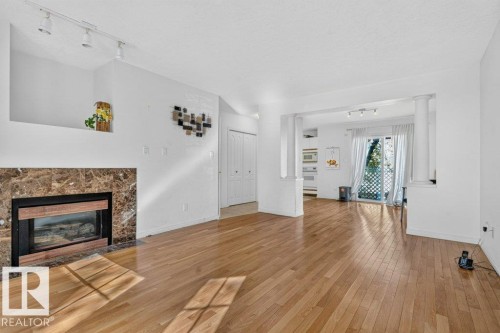 Wood-finish flooring throughout, fireplace with stone surround, recessed wall niche, track lighting, and a glass sliding door - Edmonton, AB 