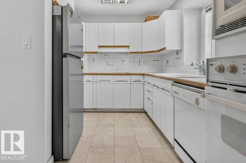 Kitchen featuring white cabinetry, wood-finish countertops, tiled flooring, a stainless steel refrigerator, and a built-in oven - Edmonton, AB 