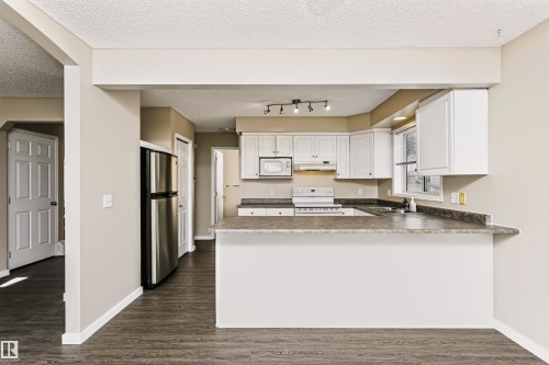 Kitchen featuring white cabinetry, gray countertops, stainless steel refrigerator, white appliances, and wood-finish flooring - 4112 37A Avenue Nw, Edmonton, AB 