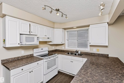 White cabinetry with dark contrasting countertops, built-in microwave, double basin sink, and wood-finish flooring - 4112 37A Avenue Nw, Edmonton, AB 