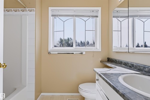 Tub-shower combination with white tile surround, vanity with a white integrated sink, and an embedded mirror - 4112 37A Avenue Nw, Edmonton, AB 