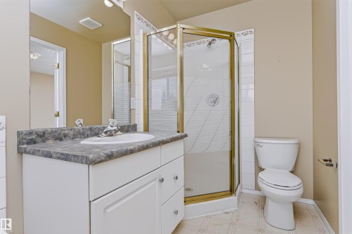 Bathroom featuring a single vanity with an integrated sink and stone-look countertop, a clear glass shower enclosure with a gold-tone frame, and a white toilet - 4112 37A Avenue Nw, Edmonton, AB 