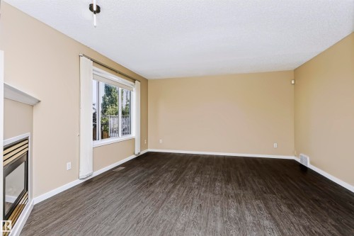 Spacious room featuring dark wood-finish flooring, a large window, a built-in fireplace, and neutral wall tones - 4112 37A Avenue Nw, Edmonton, AB 