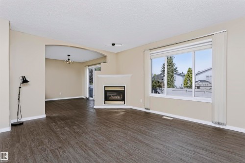 Expansive living area with wood-finish flooring, a built-in fireplace, and a large window - 4112 37A Avenue Nw, Edmonton, AB 