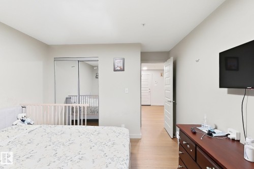Sliding mirrored closet doors, light wood-finish flooring, white paneled interior door, and light neutral wall paint - #116 4008 Savaryn Dr Sw Sw, Edmonton, AB 