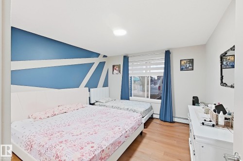 Accent wall with geometric design, wood-finish flooring, white trim, and window with blinds - #116 4008 Savaryn Dr Sw Sw, Edmonton, AB 