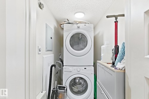 Stackable washer and dryer units, built-in cabinetry with light-toned countertop, and recessed ceiling lighting - #116 4008 Savaryn Dr Sw Sw, Edmonton, AB 