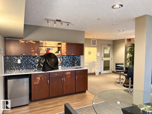 Built-in kitchenette featuring dark wood cabinetry, a mosaic tile backsplash, and a stainless steel mini-refrigerator - #116 4008 Savaryn Dr Sw Sw, Edmonton, AB 