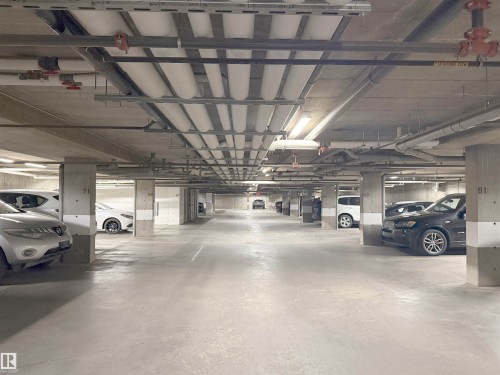 Subterranean parking garage featuring concrete pillars, exposed conduit, and integrated fluorescent lighting - #116 4008 Savaryn Dr Sw Sw, Edmonton, AB 