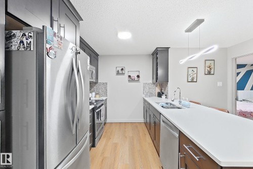 Kitchen featuring dark-finish cabinetry, stainless steel appliances, solid surface countertops, a mosaic tile backsplash, and wood-finish flooring - #116 4008 Savaryn Dr Sw Sw, Edmonton, AB 