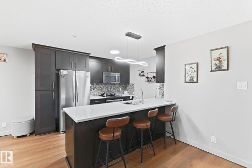 Kitchen featuring stainless steel appliances, dark wood-finish cabinetry, a white countertop island, and wood-finish flooring - #116 4008 Savaryn Dr Sw Sw, Edmonton, AB 