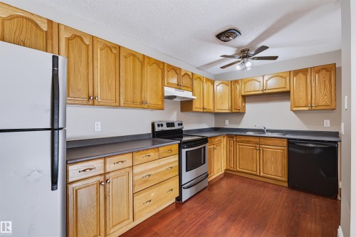 Kitchen featuring wood-finish cabinetry, dark countertops, wood-finish flooring, stainless steel range, and a ceiling fan with integrated lighting - 155 Primrose Gardens Gardens Nw, Edmonton, AB 