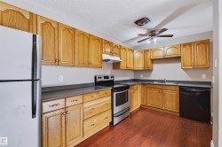 Kitchen featuring wood-finish cabinetry, dark countertops, wood-finish flooring, stainless steel range, and a ceiling fan with integrated lighting - 