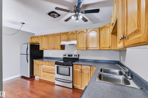 Kitchen featuring wood-finish cabinetry, stainless steel appliances, dark countertops, and wood-finish flooring - 155 Primrose Gardens Gardens Nw, Edmonton, AB 