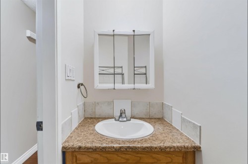 Vanity with an integrated sink, granite-look countertop, tile backsplash, and wood-finish cabinetry - 155 Primrose Gardens Gardens Nw, Edmonton, AB 