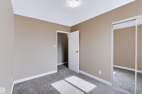 Neutral-toned walls, textured carpet flooring, white trim, interior door, and mirrored closet doors - 155 Primrose Gardens Gardens Nw, Edmonton, AB 